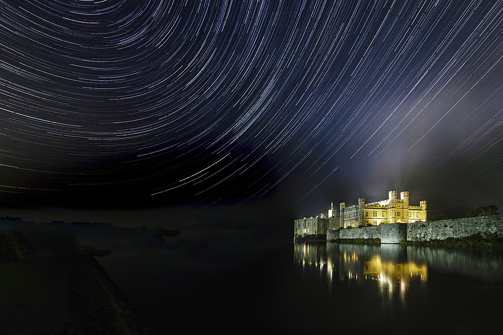 Leeds castle illuminated reflected in moat showing star trails in the night sky, near Maidstone, Kent, England, United Kingdom, Europe