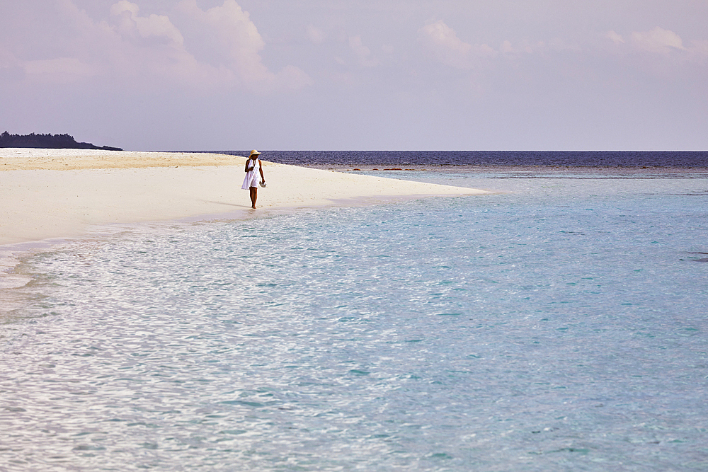 Walking close to the water's edge, as pristine shallow waters lap against the white coral sand of a tropical beach; Havodda Island, in the far south of the Maldives, Gaafu Dhaalu atoll, Indian Ocean.