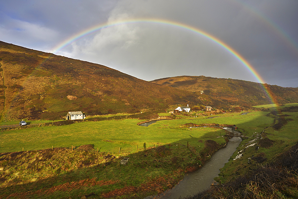 A valley rainbow forms in the face of an autumn squall, in Duckpool, a remote cove near Bude, north coast of Cornwall, England, United Kingdom, Europe