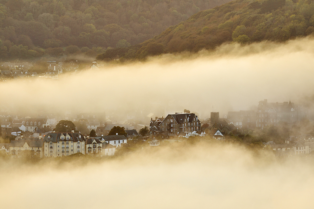 Sea fog envelops the coastal town of Lynton, lit by the light of sunset, seen from Countisbury Hill, Exmoor National Park, Devon, England, United Kingdom, Europe