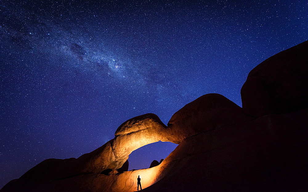 Tourist under the Rock Arch bridge in the Spitzkoppe region with a view of the Milky Way, Erongo region, Namibia, Africa