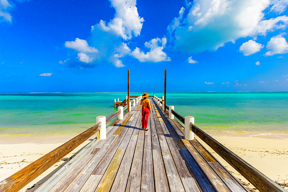 Woman walking up the pier that stretches out into the ocean from Horse Stable Beach, North Caicos, Turks and Caicos Islands, Atlantic, Central America