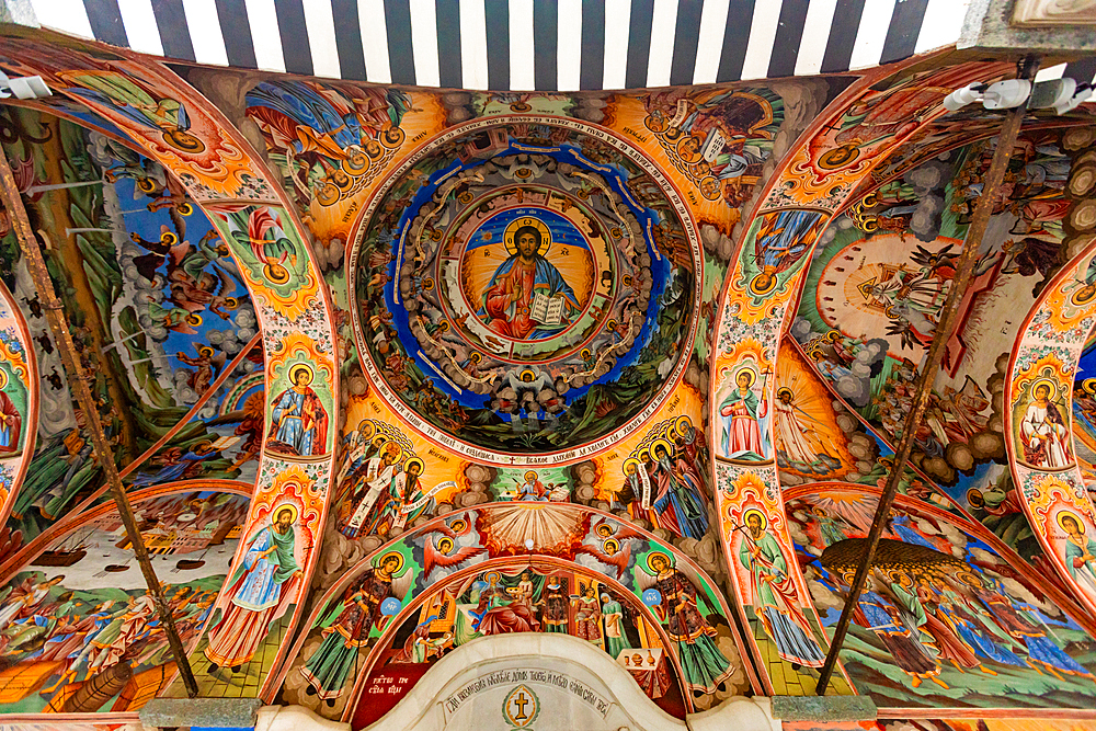 Horizontal, upward shot of the painted ceiling in the portico of the main church at Rila Monastery in Rila, Bulgaria, depicting detailed Orthodox Christian frescoes with religious scenes and figures.