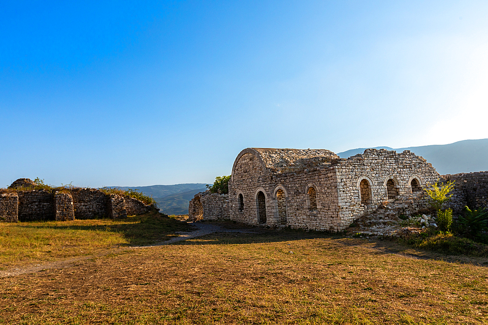 Stone remains of a Byzantine church within the fortified grounds of Kala Castle in Berat, Berat County, Albania, surrounded by mountain views and open grassy terrain.