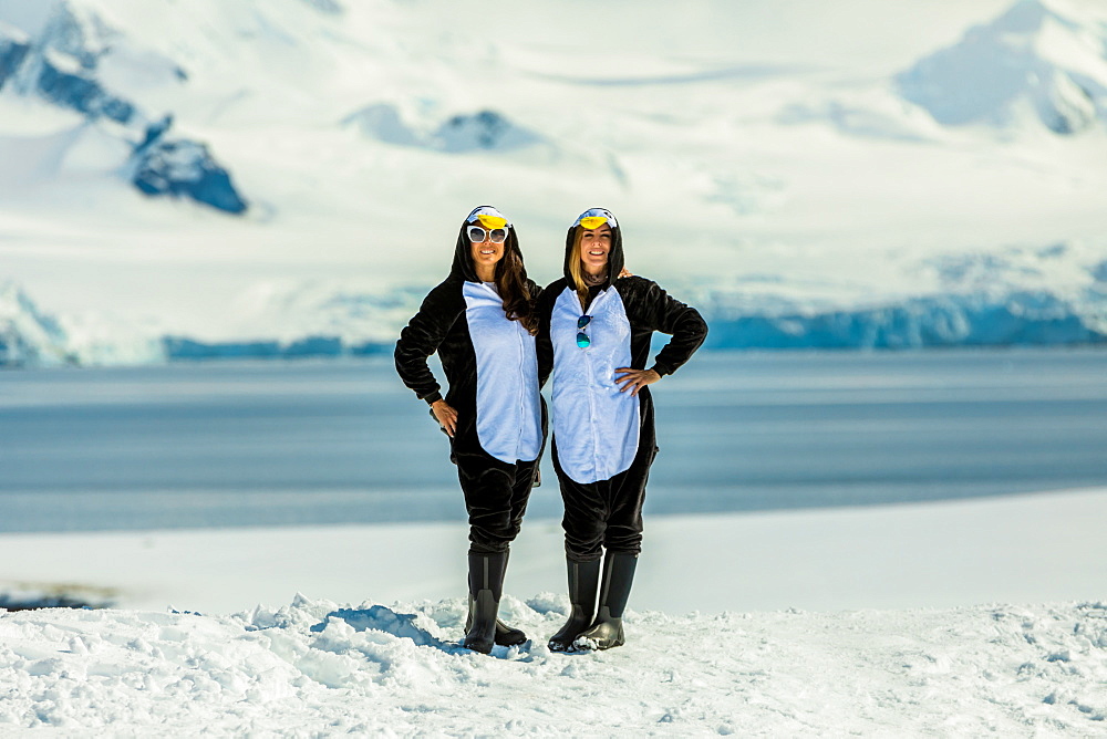 Two American women tourists in Penguin Onesies on sunny day, posing on the glaciers, Antarctica, Polar Regions