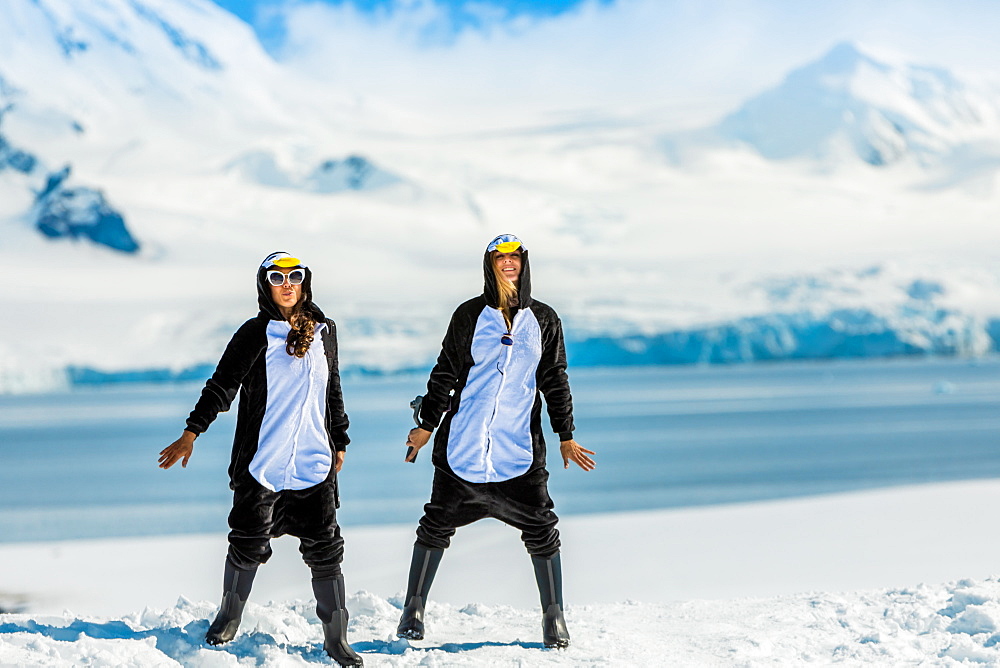 Two American women tourists in Penguin Onesies on sunny day, posing on the glaciers, Antarctica, Polar Regions