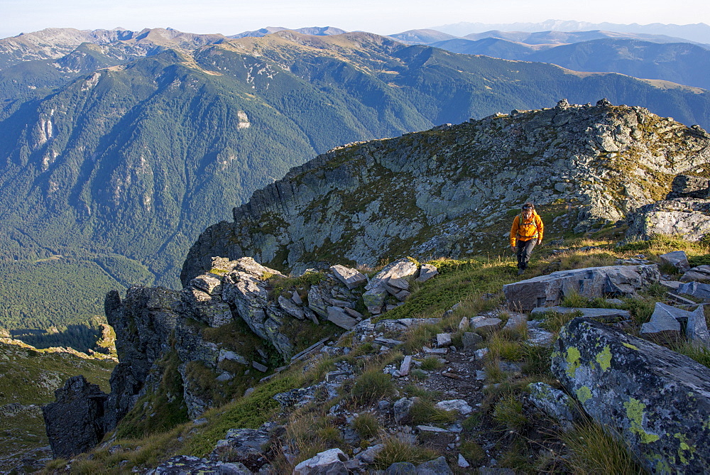 A hiker climbs along a high ridge near Maliovitsa in the Rila Mountains with distant views of valleys and hills, Bulgaria, Europe