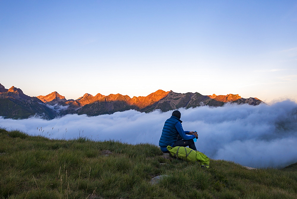 A hiker watches the sunset on the Pyrenees and a cloud inversion near Refuge Pombie along the GR10 trekking route, Pyrenees Atlantiques, France, Europe