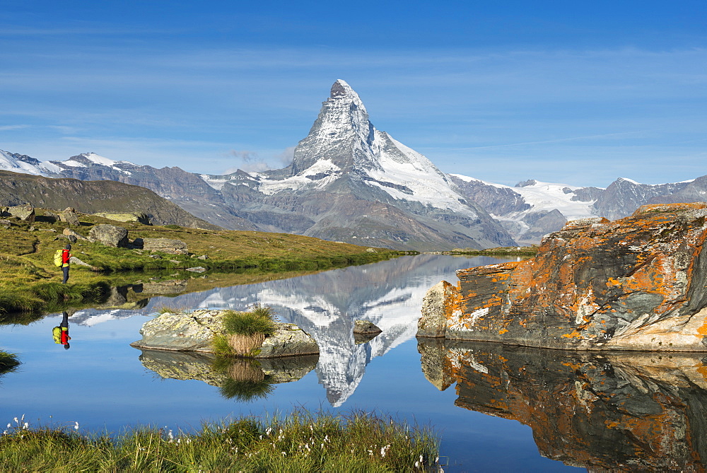 A walker hiking in the Alps takes in the view of the Matterhorn reflected in Stellisee lake at dawn, Swiss Alps, Switzerland, Europe