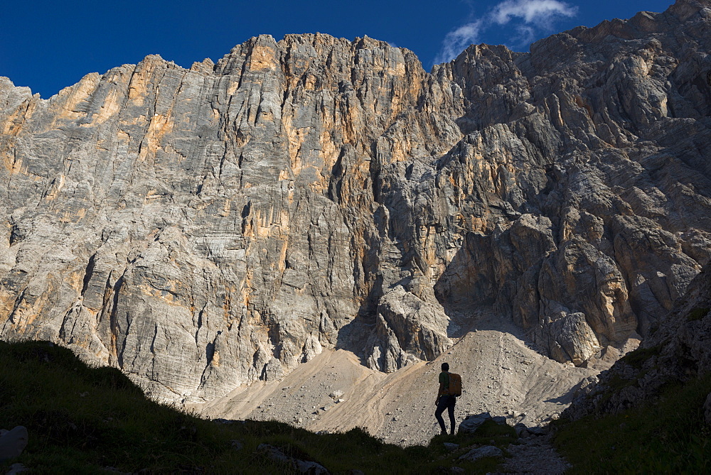 A trekker takes a break from the trail under the impressive northwest vertical wall of Monte Civetta in the Dolomites, Belluno, Veneto, Italy, Europe