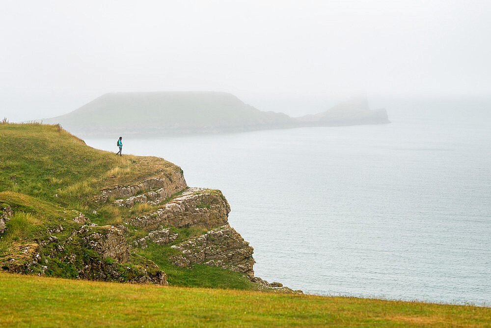 A woman looking towards Worms Head on The Gower peninsula on a misty day, Wales, United Kingdom, Europe