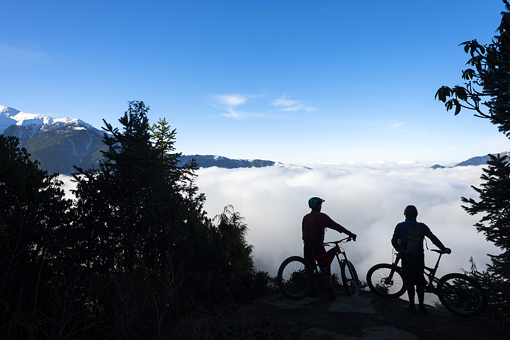 Mountain bikers look out across a valley filled with a cloud inversion in the Himalayas while biking in the Gosainkund region, Langtang region, Nepal, Asia