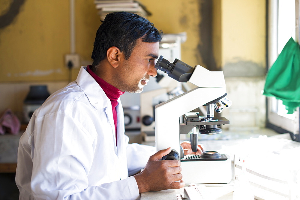 A lab technician working in a laboratory in a small hospital in Nepal looks into a microscope, Jiri, Solu Khumbu, Nepal, Asia