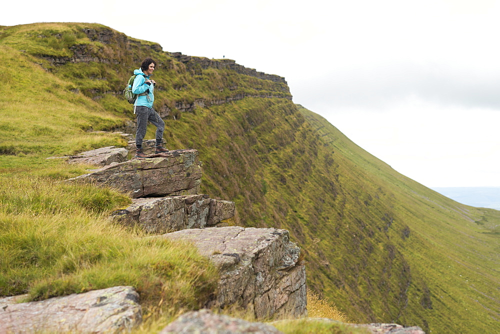 A woman looks out from a ridge while walking to Lyn y Fan Fawr in the Brecon Beacons, South Wales, United Kingdom, Europe