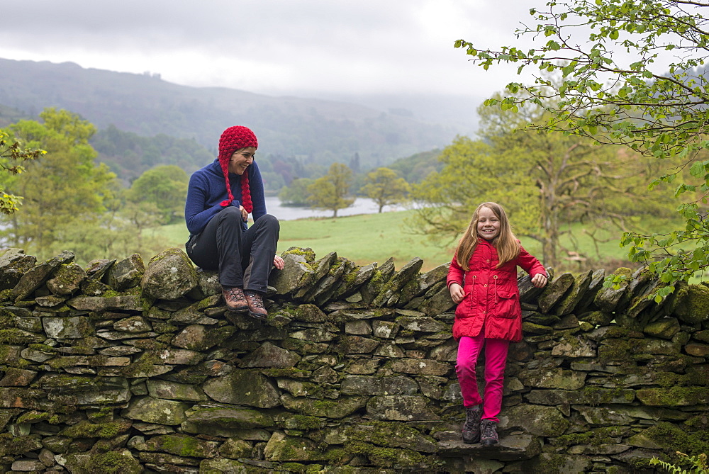 Mother and daughter rest on a dry stone wall while on holiday in the Lake District, Cumbria, England, United Kingdom, Europe