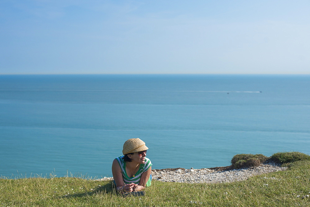 A woman lies on the cliffs near Beachy Head with views of the sea in the distance, East Sussex, England, United Kingdom, Europe