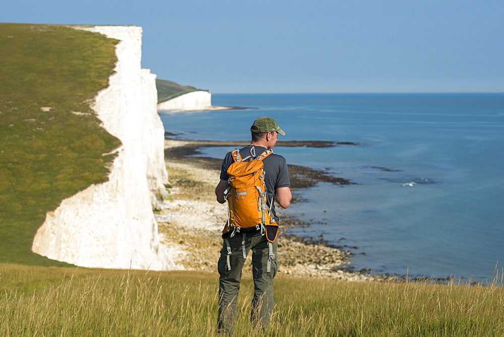 A man looks out over the chalk cliffs with views of the Seven Sisters coastline in the distance, South Downs National Park, East Sussex, England, United Kingdom, Europe