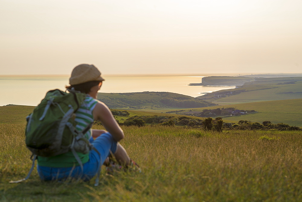 A woman looks out to sea near Beachy Head with views of the Seven Sisters coastline in the distance, South Downs National Park, East Sussex, England, United Kingdom, Europe