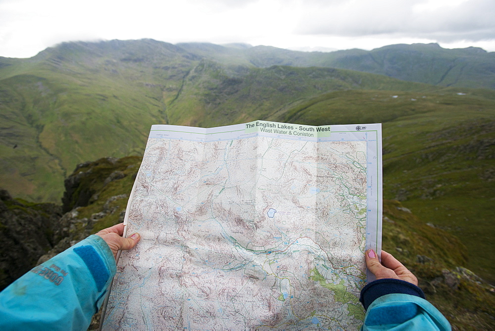 A woman checks her map while looking towards Great Langdale valley from the Langdale Pikes, Lake District, Cumbria, England, United Kingdom, Europe