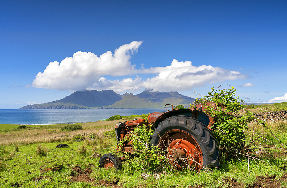 An abandoned tractor on a Cleadale Croft, with distant view of The Isle of Rhum in mid-summer, Cleadale, Island of Eigg, Small Isles, Inner Hebrides, Scotland, United Kingdom, Europe