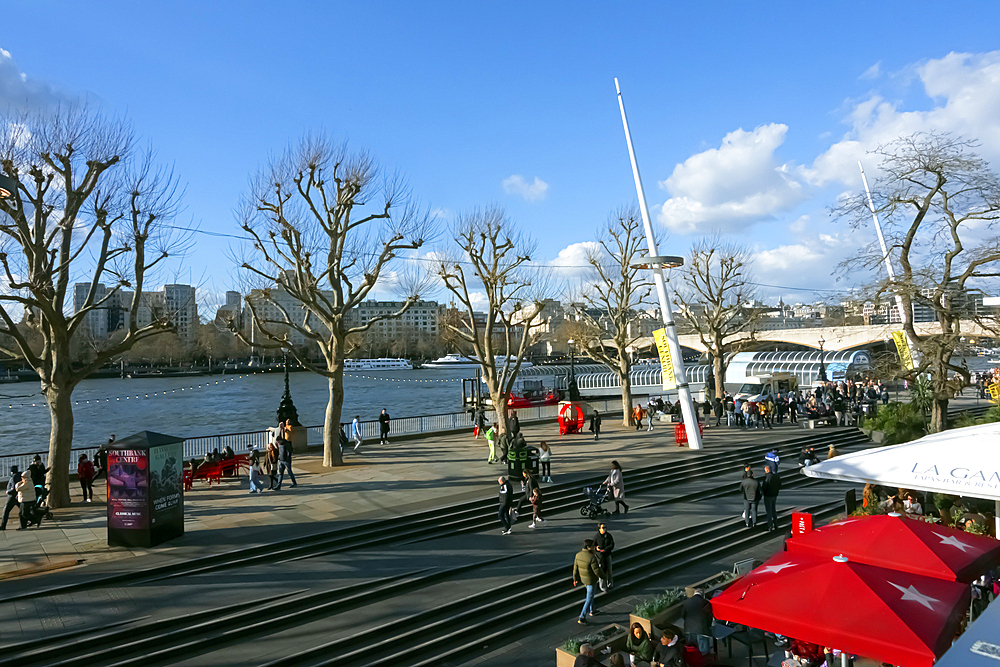 People stroll and picnic along the South Bank of the River Thames close to the Royal Festival Hall, London, England, United Kingdom, Europe