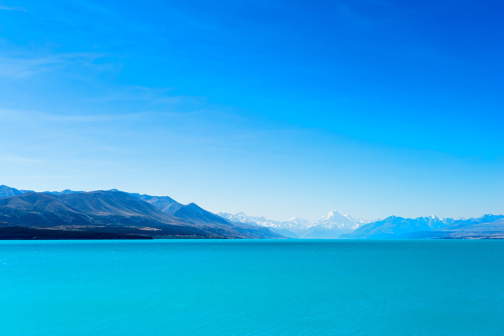 A turquoise blue lake with snow covered mountains in the distance, South Island, New Zealand, Pacific