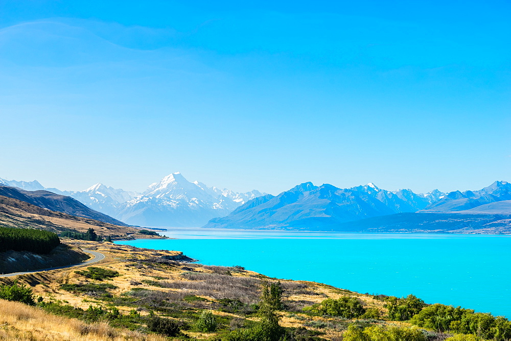 A road winds along the edge of a turquoise blue lake with mountains in the distance, South Island, New Zealand, Pacific