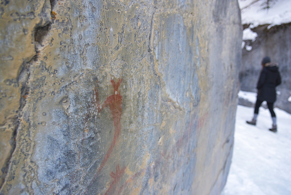 Ancient native pictographs (cave paintings) on a canyon wall with a young woman walking in background, Grotto Canyon, Alberta, Canada, North America