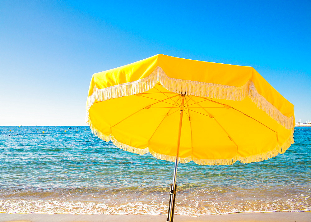 Giant yellow beach umbrella next to the ocean against a blue sky in Juan les Pins, Cote d'Azur, Provence, France, Mediterranean, Europe