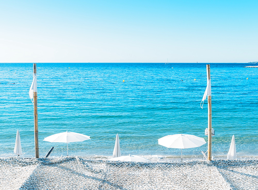 Giant white beach umbrella next to the ocean against a blue sky in Juan les Pins, Cote d'Azur, Provence, France, Mediterranean, Europe