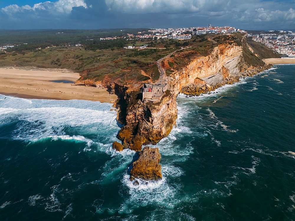 Aerial view of tourists at the historic Sao Miguel Arcanjo lighthouse overlooking Nazare's stunning coastline with giant waves, enjoying spectacular views, Nazare, Oeste, Estremadura, Portugal, Europe