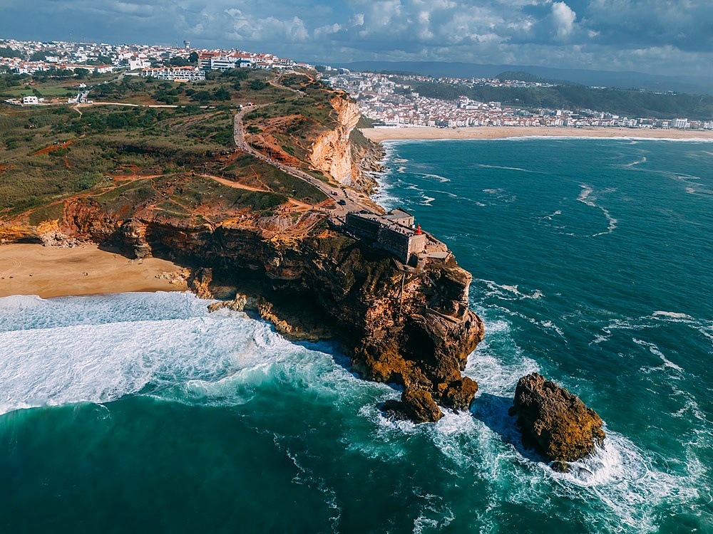 Aerial view of tourists at the historic Sao Miguel Arcanjo lighthouse overlooking Nazare's stunning coastline with giant waves, enjoying spectacular views, Nazare, Oeste, Estremadura, Portugal, Europe