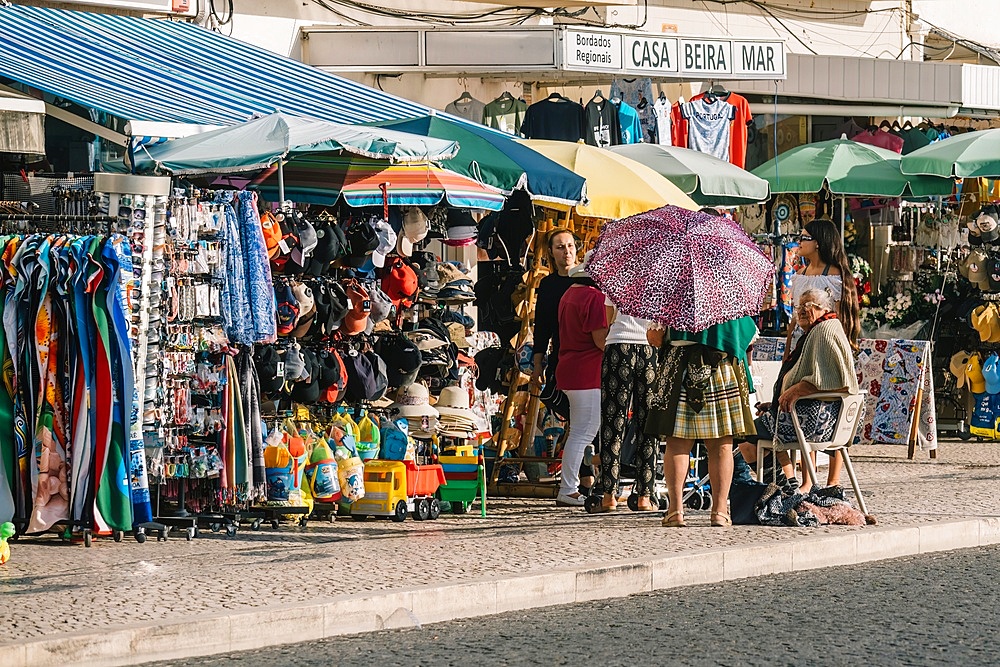 Local vendors chat, and stalls with array of colourful goods, in the vibrant marketplace of Nazare, Oeste, Estremadura, Portugal, Europe