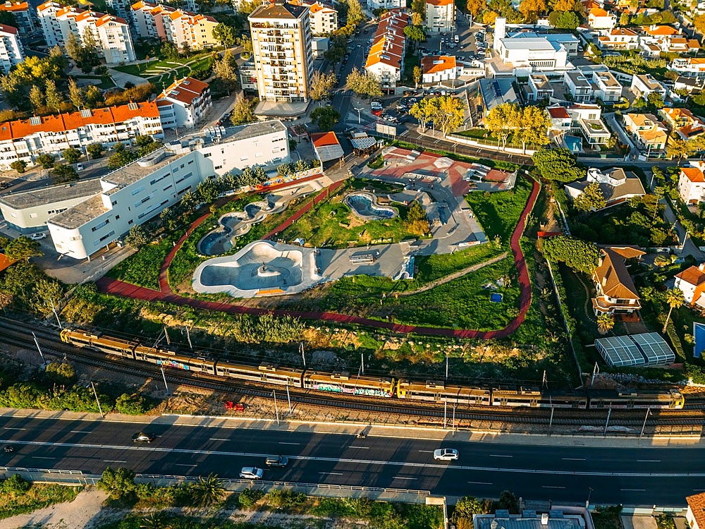 Aerial drone view of skateboard Parque das Geracoes, with Comboio de Portugal train in the foreground on the Cascais Line, in Sao Joao do Estoril, Portugal, Europe