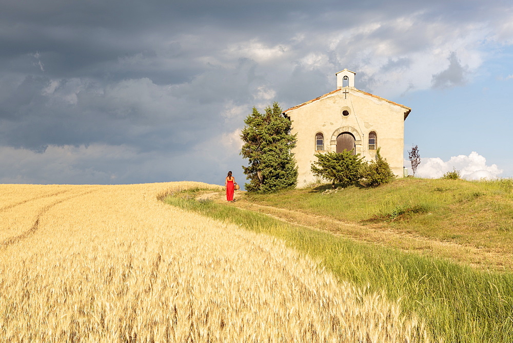 Woman in red dress and wicker basket passing by Notre-Dame-de-Sante chapel, Entrevennes, Alpes-de-Haute-Provence, Provence-Alpes Cote d'Azur, France, Europe