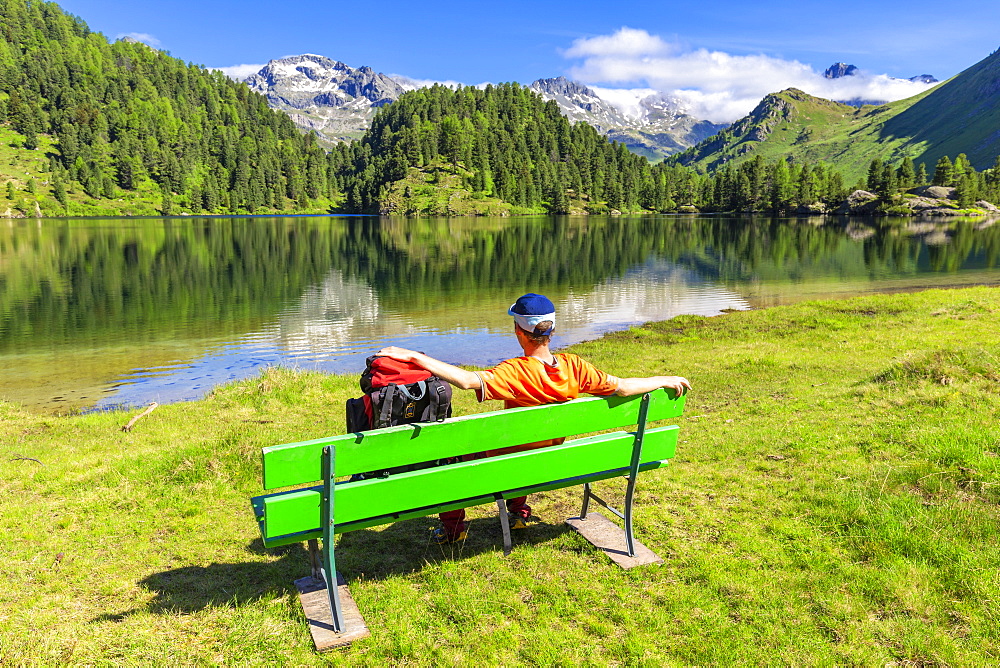 Hiker with rucksack relaxes on a bench, Lake Cavloc, Forno Valley, Maloja Pass, Engadine, Graubunden, Switzerland, Europe