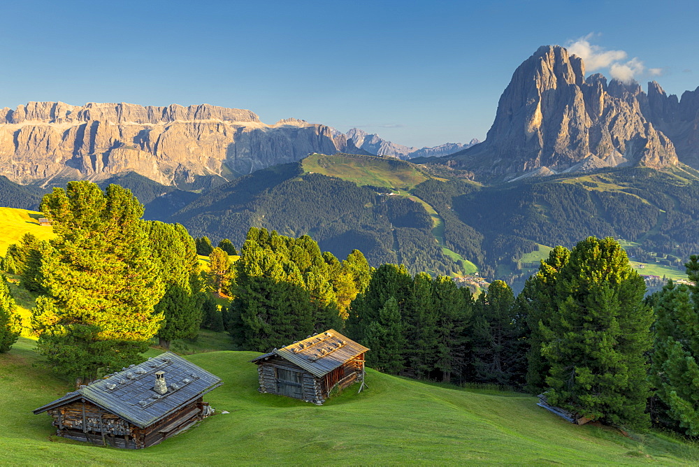 Last rays of sun on traditional huts with view on Sassolungo and Sella Group, Gardena Valley, South Tyrol, Dolomites, Italy, Europe