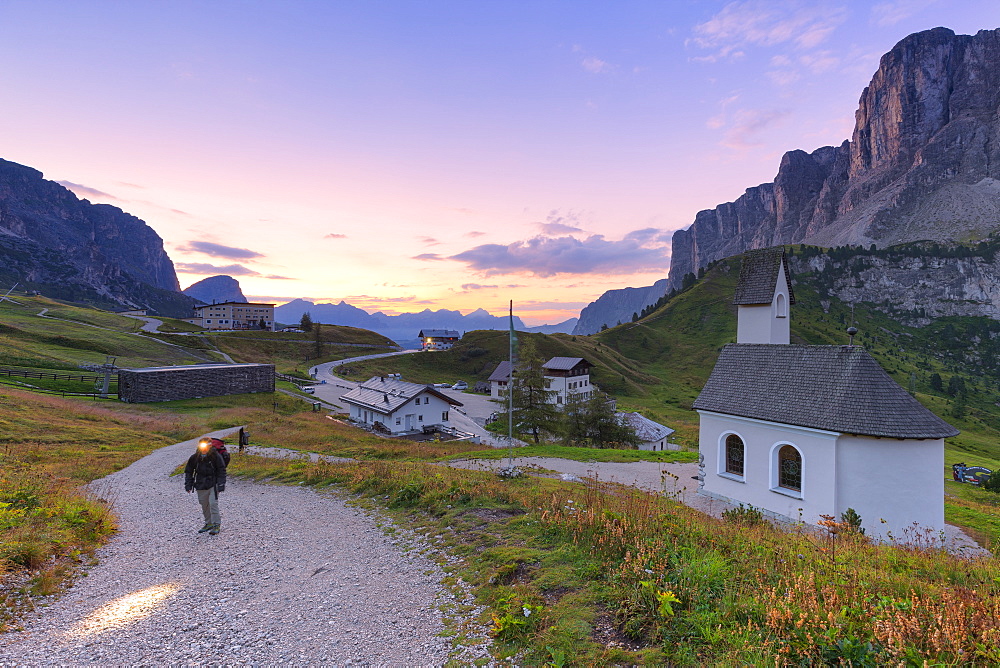 Hiker walks on a track during sunrise, Gardena Pass, Gardena Valley, South Tyrol, Dolomites, Italy, Europe