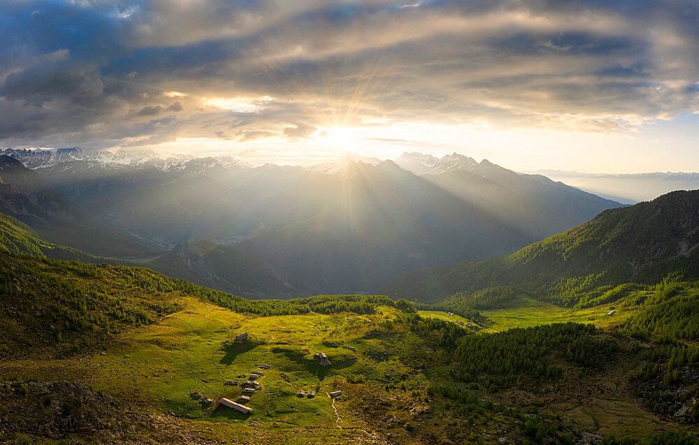 Sun filters between clouds at sunrise with illuminated pasture, Valmalenco, Valtellina, Lombardy, Italy, Europe