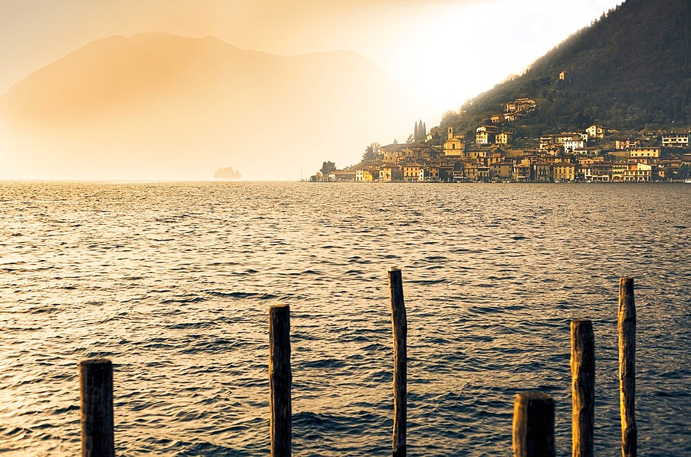 Light in the fog illuminates Peschiera Maraglio village, Monte Isola, Lake Iseo, Brescia province, Lombardy, Italian Lakes, Italy, Europe