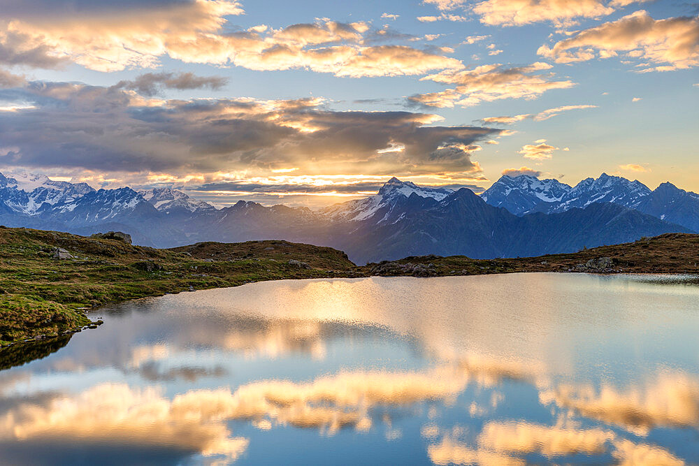 The sun and clouds is reflected in the Arcoglio Lake at sunrise, Valmalenco, Valtellina, Lombardy, Italy, Europe