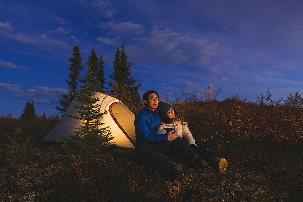 Couple sitting in front of an illuminated tent, Alaska, United States of America, North America