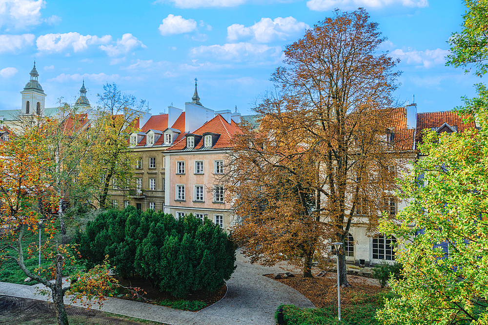 View of traditional low-rise roof-tiled houses behind a park area under blue sky with clouds, Warsaw, Poland, Europe