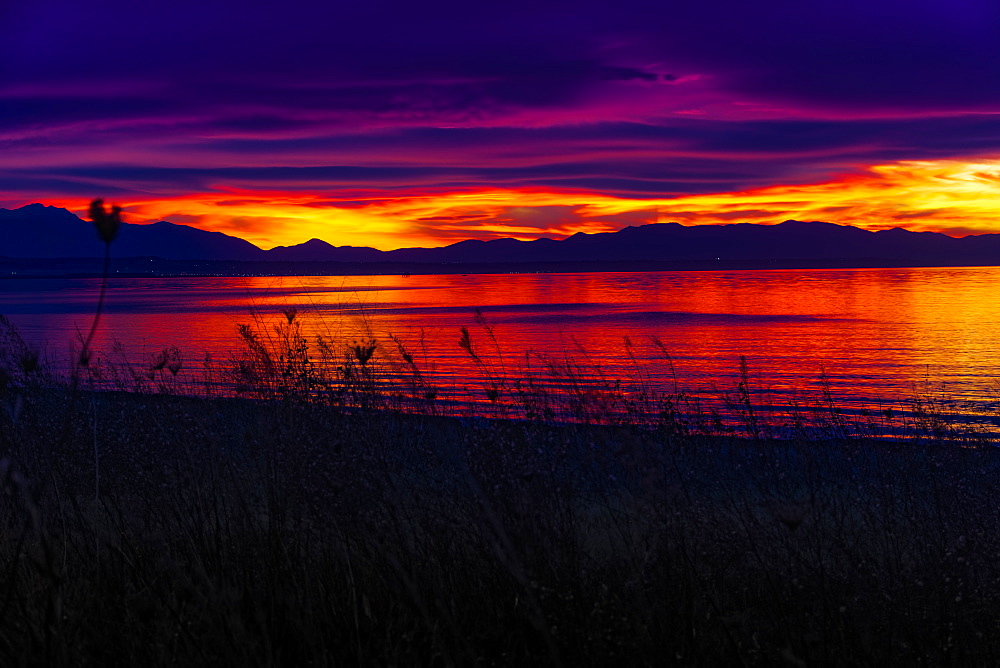 Mediterranean sunset over calm sea, orange and purple clouds over mountainous landscape silhouette, Greece, Europe