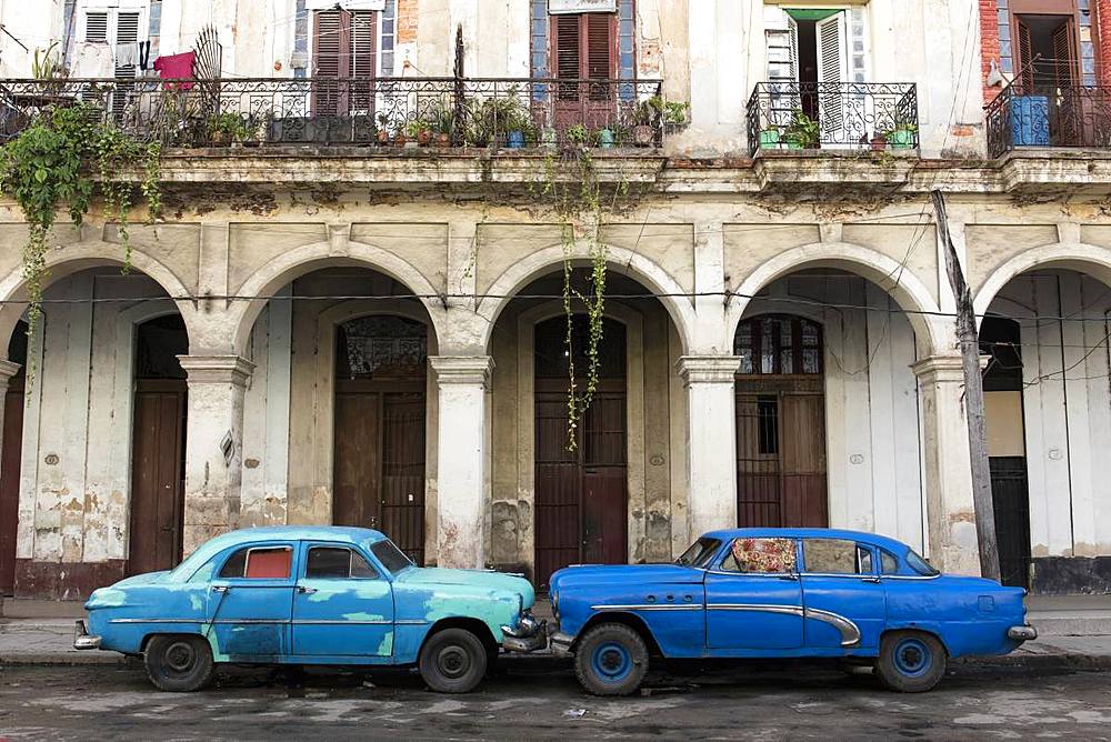 Two blue cars face nose to nose outside a dilapidated building, Havana, Cuba, West Indies, Caribbean, Central America