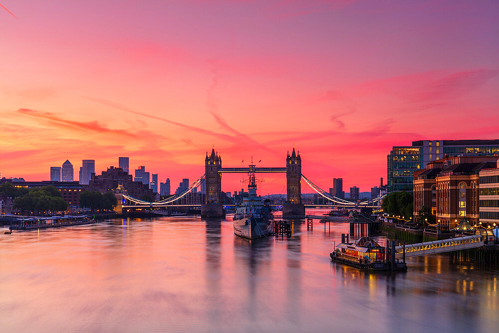 Tower Bridge, River Thames and HMS Belfast at sunrise with pink sky, and Canary Wharf in background, London, England, United Kingdom, Europe