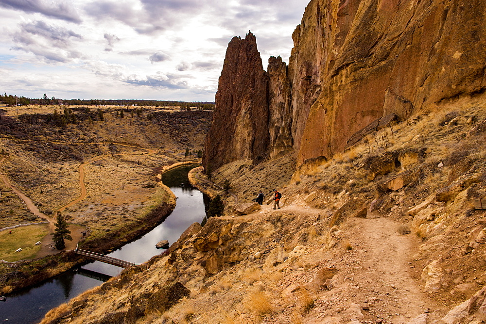 Two hikers descend a path to the river by some large rock formations, Oregon, United States of America, North America