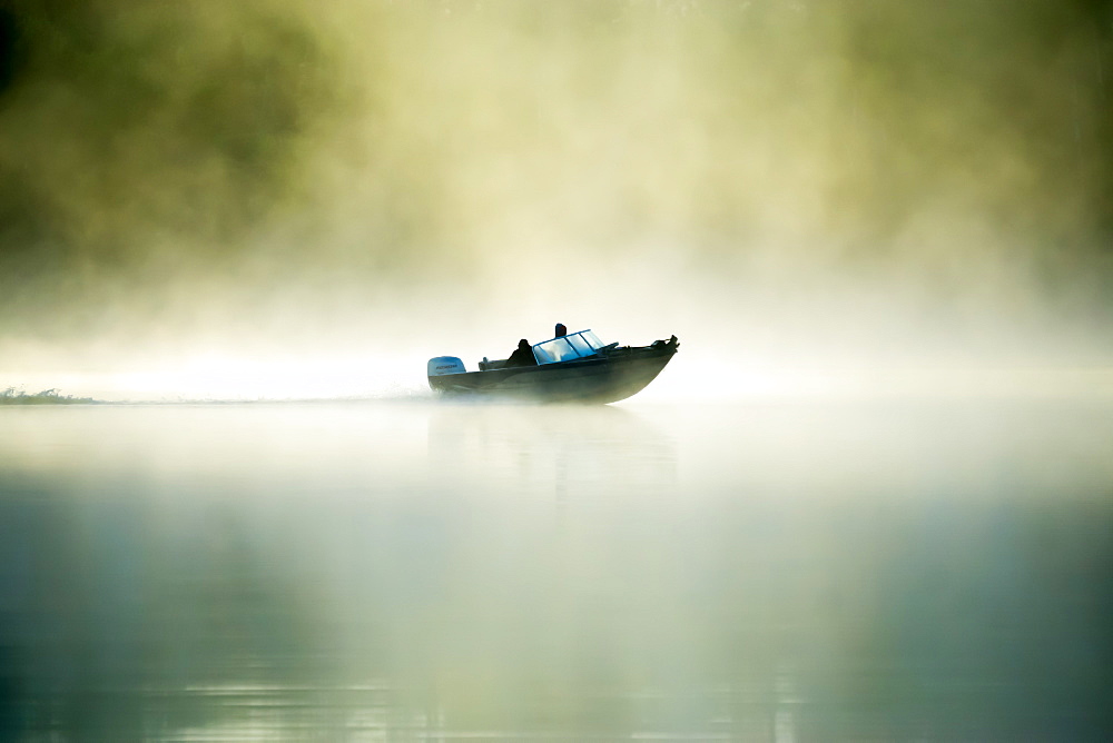 A motorboat navigates the fog on a Minnesota Lake during an early morning, Minnesota, United States of America, North America