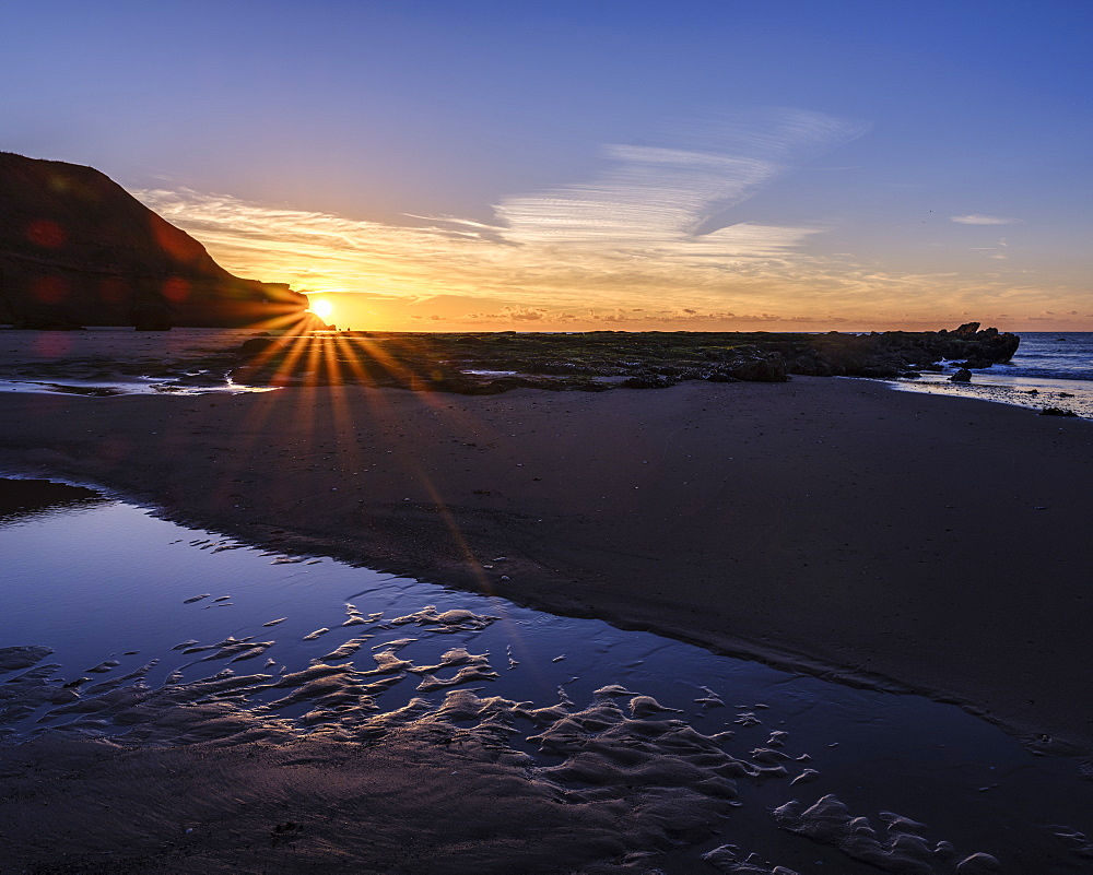 Sunstar peeping around the cliffs with a pool on the beach at Orcombe Point, Exmouth, Devon, England, United Kingdom, Europe