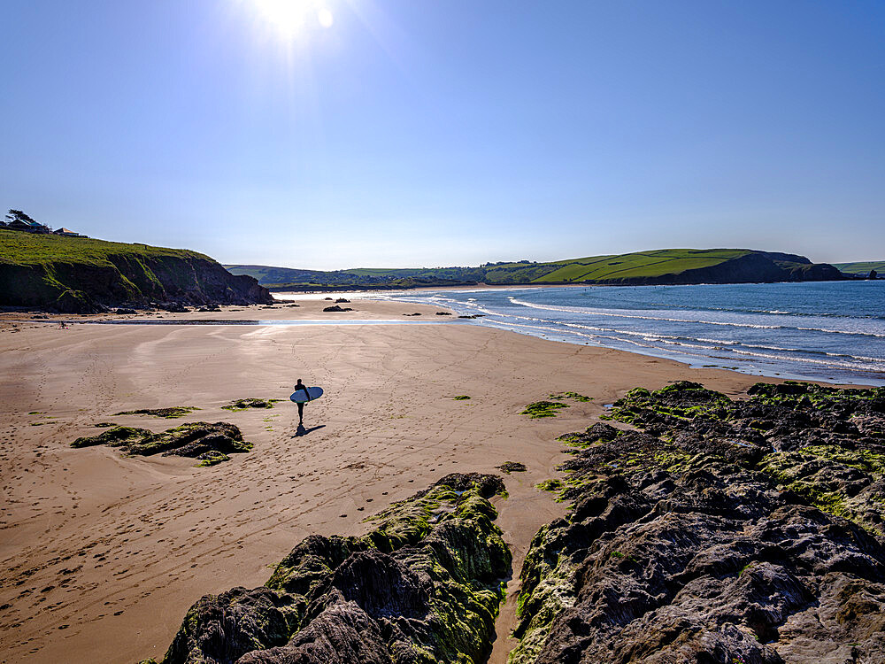 A surfer walks towards his session on a sunny morning at Bigbury-on-Sea, Devon, England, United Kingdom, Europe